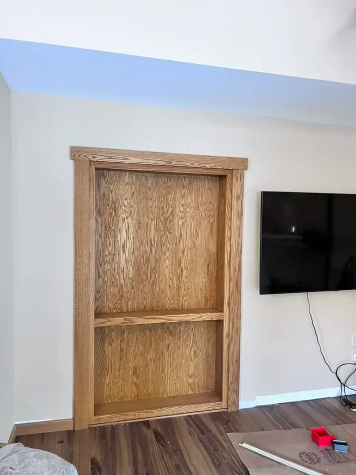 Oak built-in bookcase with open shelves and oak trim, set into a living room wall beside a wall-mounted TV