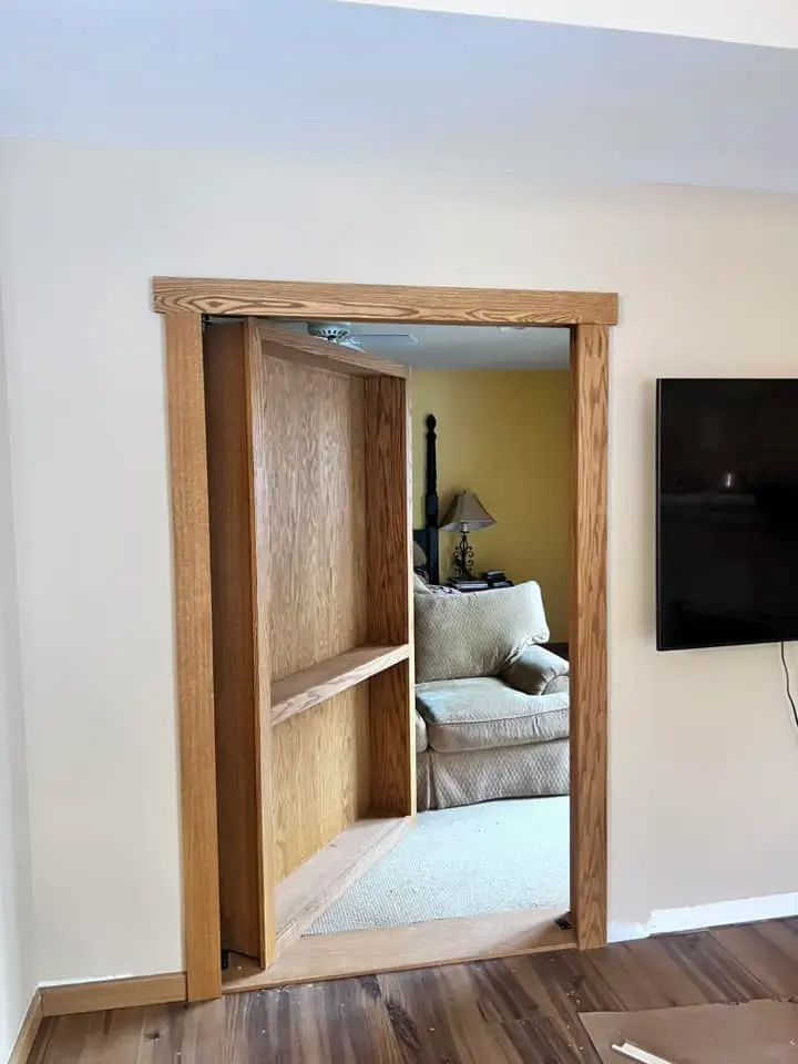 Oak built-in bookcase standing open as a hidden door, revealing a passage behind the shelves.
